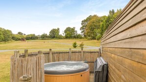 A wooden deck with a hot tub and a covered grill area, surrounded by a wooden fence and a grassy yard. - 1 Bed in Lampeter (oc-78189) (Lampeter)