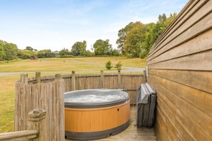 A wooden deck with a hot tub and a covered grill area, surrounded by a wooden fence and a grassy yard.