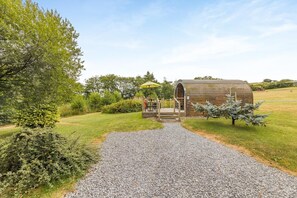 Une construction rustique en bois, accessible par un chemin de gravier, et entourée de verdure.