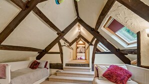 Un dormitorio tipo loft con vigas de madera a la vista, un tragaluz y una escalera que lleva a un nivel superior.
