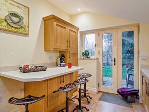 A kitchen with wooden cabinets, a coffee maker, and a red mug on the counter. There are two bar stools and a small table. - 2 Bed in Coleford (oc-78181) (English Bicknor)