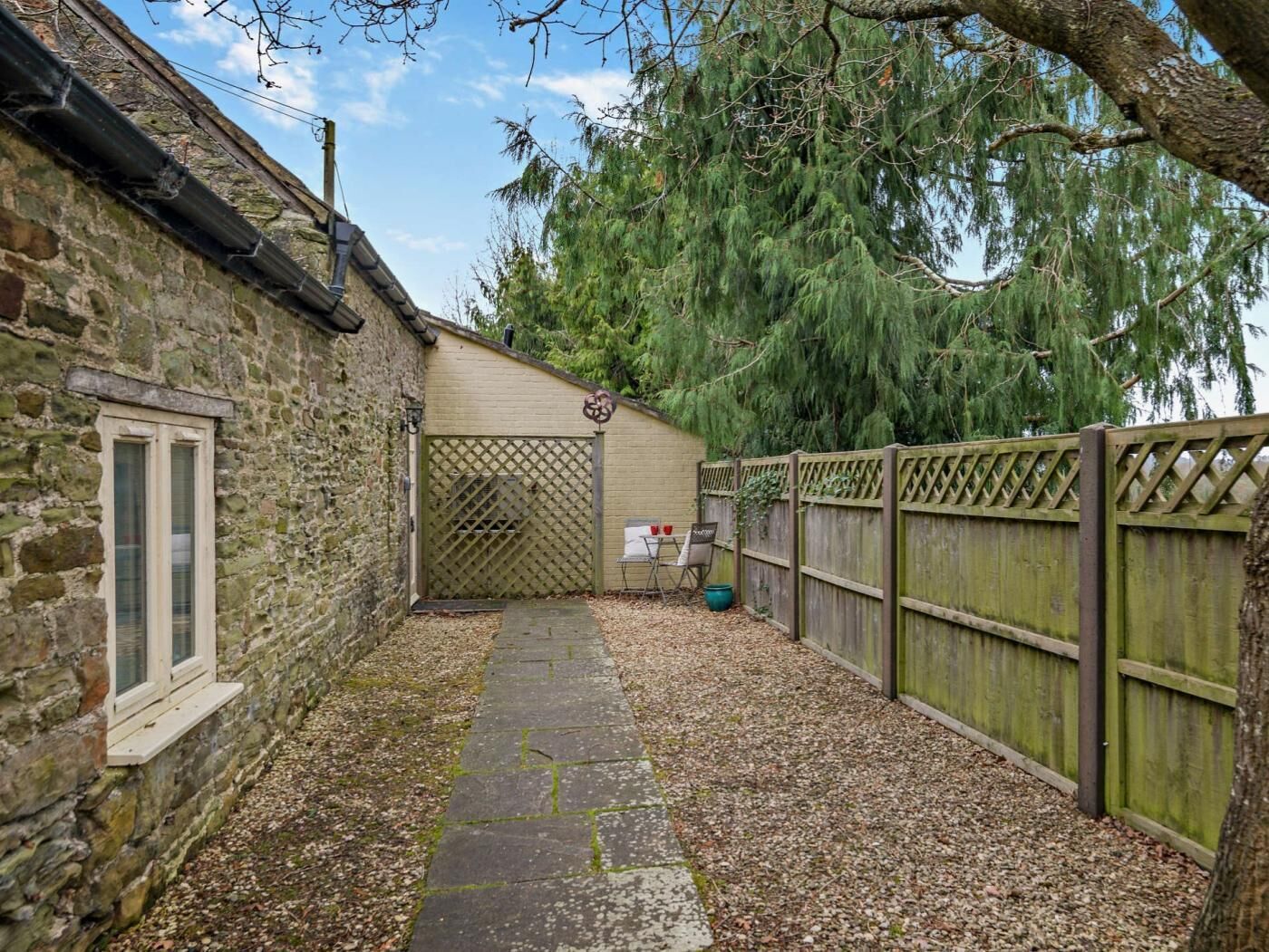 A stone building with a window, a wooden fence, and a paved pathway.