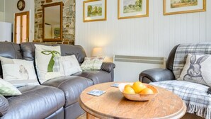 Ein Wohnzimmer mit zwei Ledersofas, einem Holztisch mit Früchten, gerahmten Kunstwerken an der Wand und einer Steinwand.