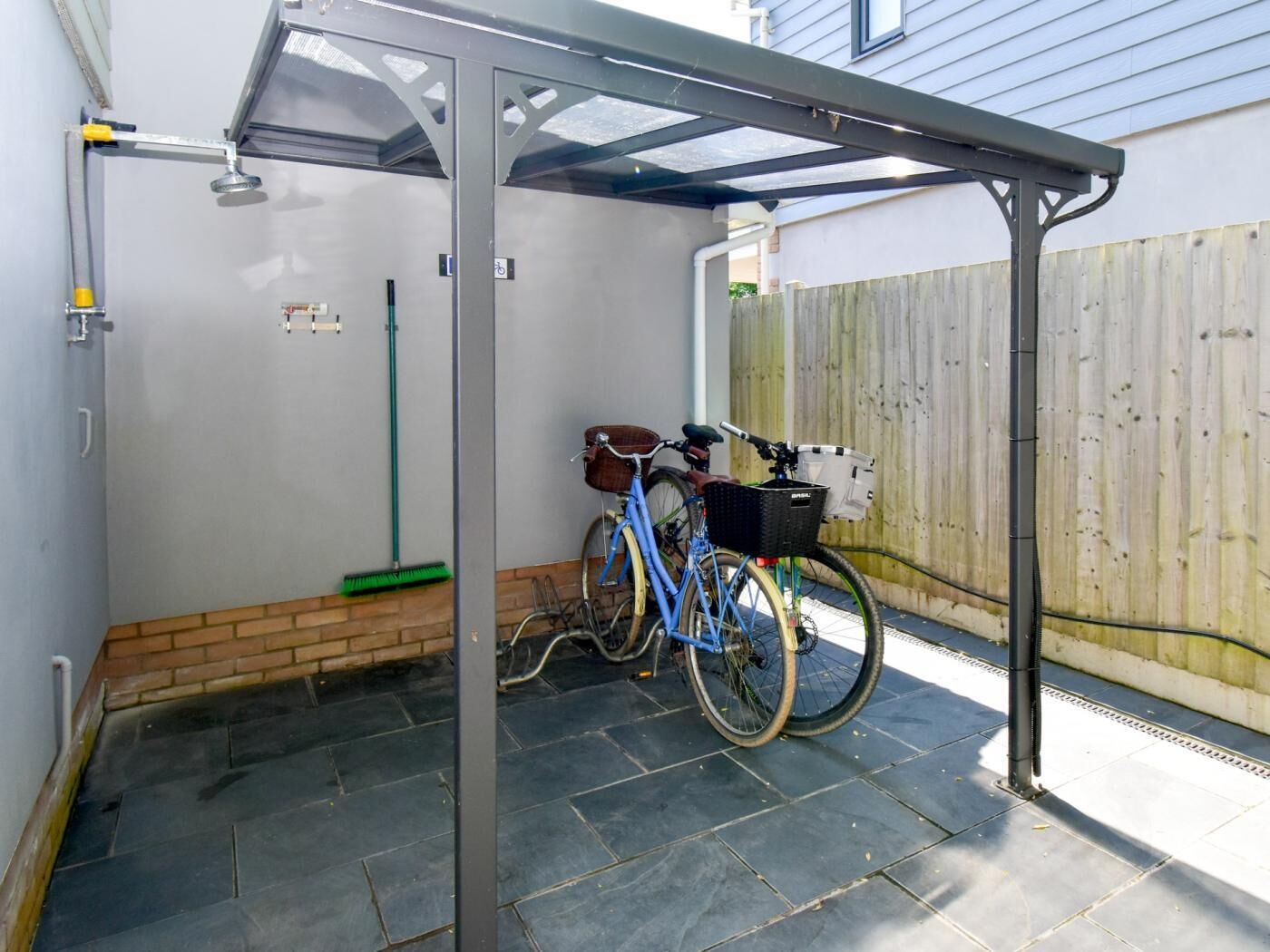 A covered patio area with a bicycle, a broom, and a trash bin.