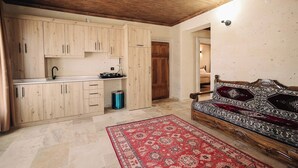 Una cocina con armarios de madera, un fregadero y una estufa. Hay un tapete rojo estampado en el suelo y un sofá con un cojín estampado.