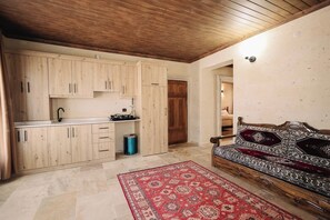 A kitchen with wooden cabinets, a sink, and a stove. There is a red patterned rug on the floor and a sofa with a patterned cushion. - Castle Stone House (Nevsehir)