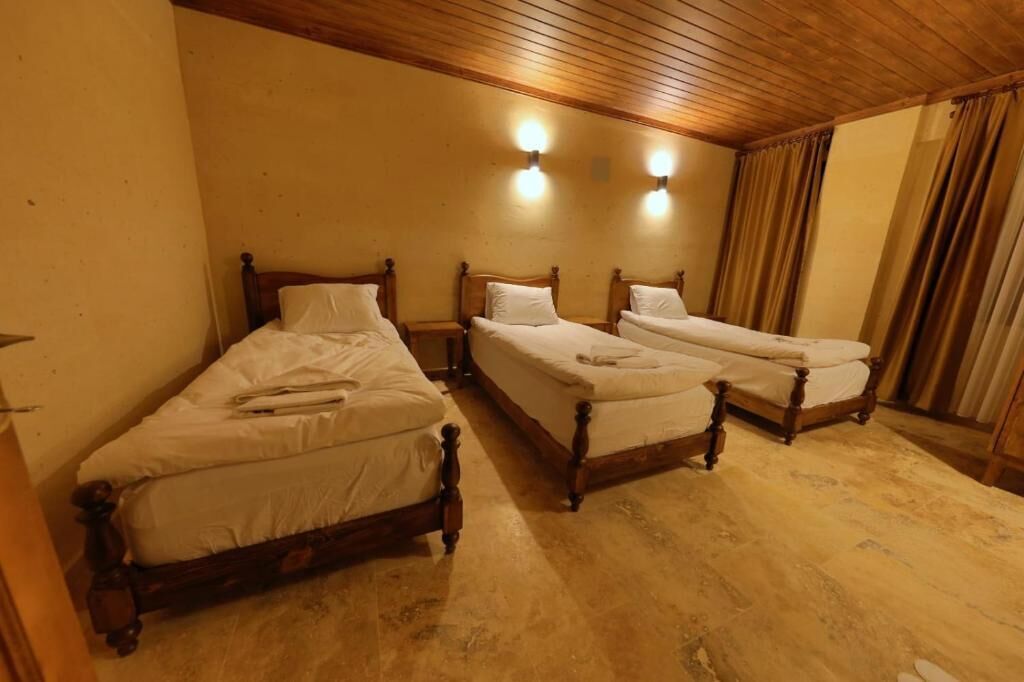 A room with three wooden beds, each with a wooden headboard and white bedding. There are two wall-mounted light fixtures above the beds.