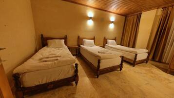 A room with three wooden beds, each with a wooden headboard and white bedding. There are two wall-mounted light fixtures above the beds.