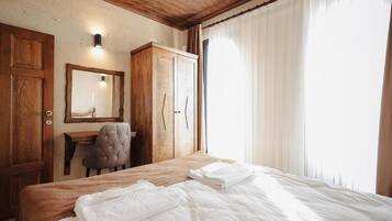 Een slaapkamer met een houten bed, een bureau met stoel, een kledingkast en een spiegel aan de muur.