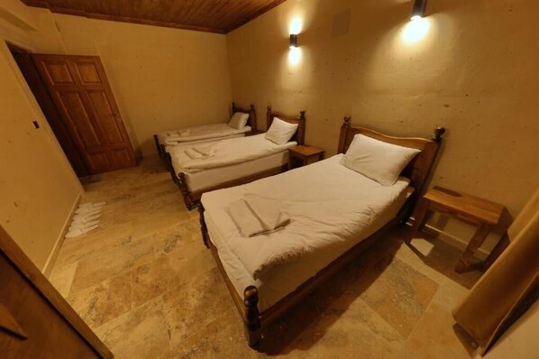 A room with three wooden beds, each with a wooden headboard and a nightstand. The room has a tiled floor and a wooden door. - Castle Stone House (Nevsehir)