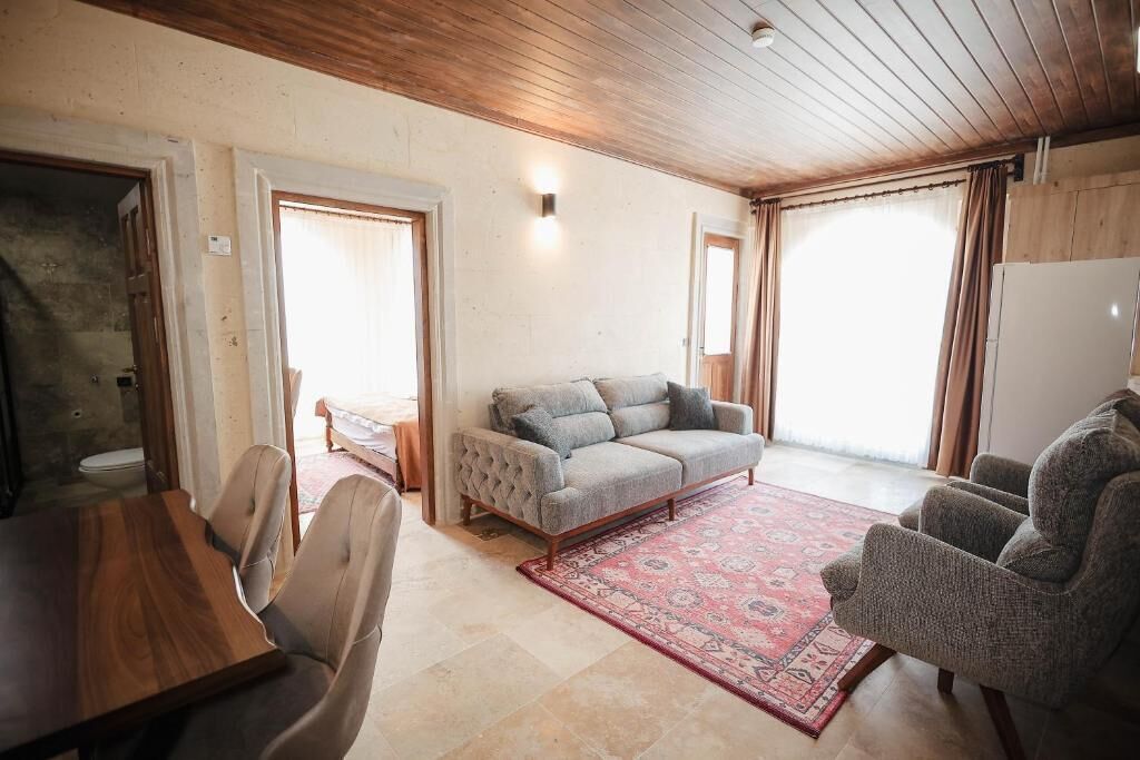 Una habitación con techo de madera, un sofá gris, un tapiz estampado y una mesa de comedor con sillas.