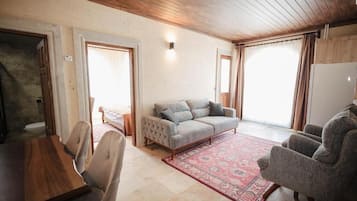 Una habitación con techo de madera, un sofá gris, un tapiz estampado y una mesa de comedor con sillas.