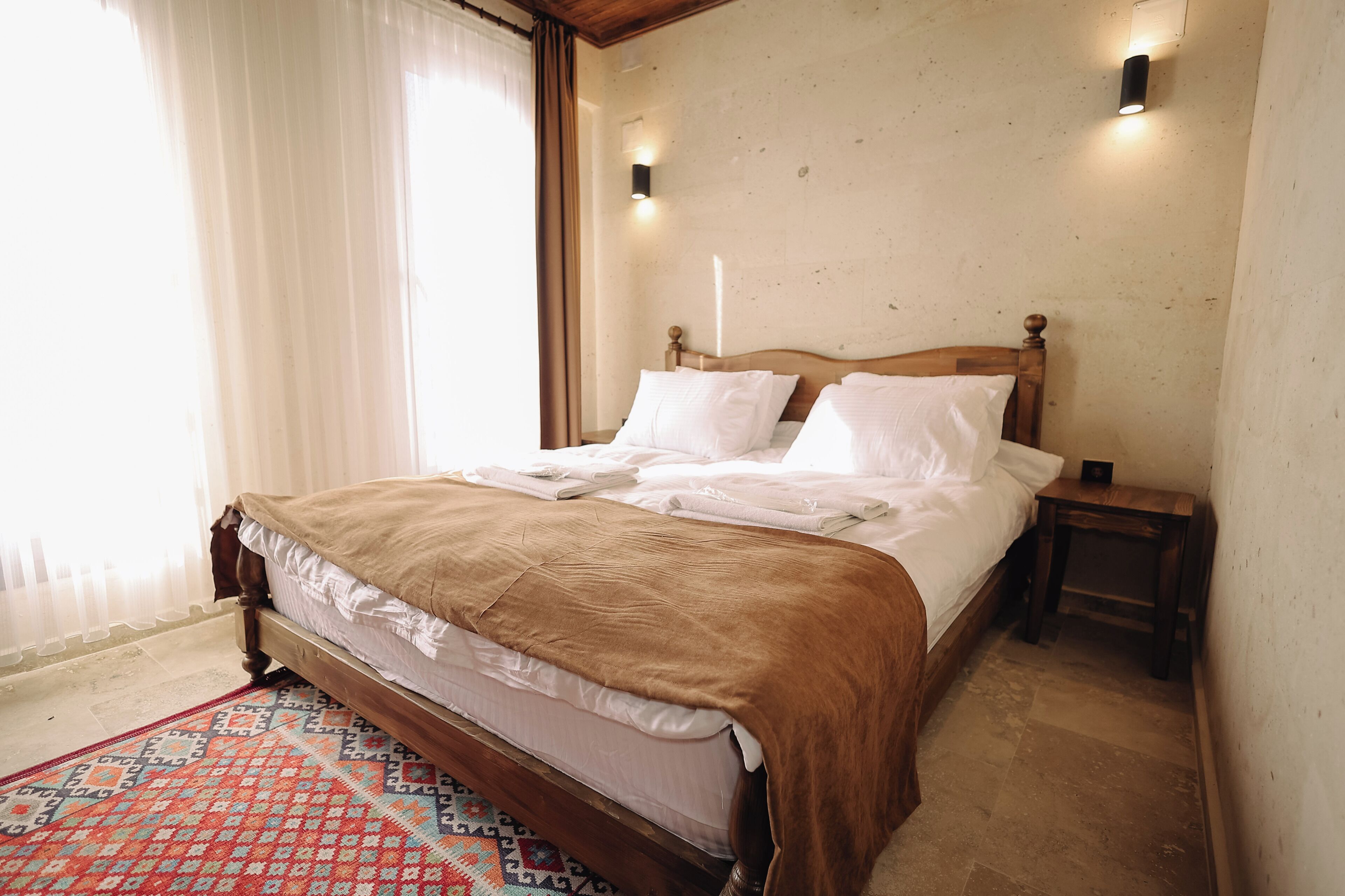 A neatly made bed with a brown blanket, a patterned rug, and two bedside tables with lamps.