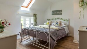 Une chambre avec un puits de lumière, un lit agrémenté de coussins décoratifs, une table de chevet et une plante suspendue.