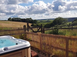 A hot tub in a fenced outdoor area with a view of rolling hills and a partly cloudy sky. - 3 Bed in Umberleigh (oc-78304) (Kings Nympton)