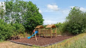 Une aire de jeux avec un toboggan et deux cabanes en bois.