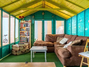Ein gemütliches Zimmer mit einer braunen Couch, einem kleinen Tisch, einem Bücherregal und einem Fenster, vor dem ein Fahrrad steht.