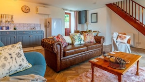 Un salon avec un canapé en cuir marron, un fauteuil bleu, une table basse en bois et un escalier.