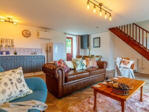 Ein Wohnzimmer mit einem braunen Ledersofa, einem blauen Sessel, einem Holztisch und einer Treppe.