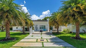 Una casa moderna con un camino de piedra que lleva a la entrada, rodeada de palmeras.