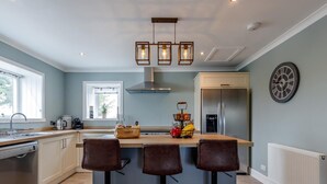 A modern kitchen with a central island, bar stools, a stainless steel refrigerator, and a clock on the wall. - 3 Bed in Crieff (oc-78313) (Madderty)