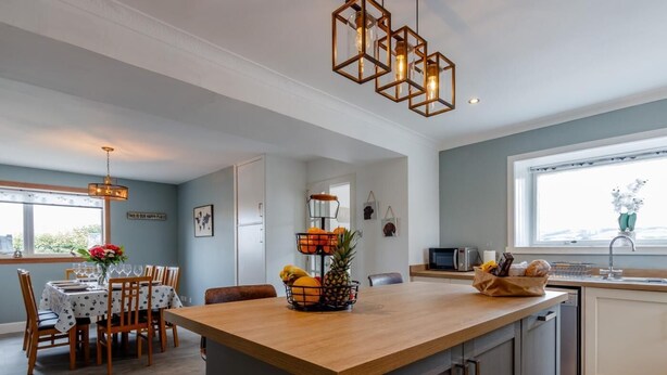 A modern kitchen with a central island, wooden cabinetry, and a dining area with a table and chairs. - 3 Bed in Crieff (oc-78313) (Madderty)