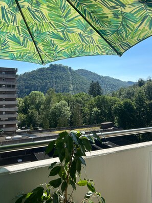 Ein Balkon mit Blick auf einen bewaldeten Hügel, ein Gebäude und eine Straße.