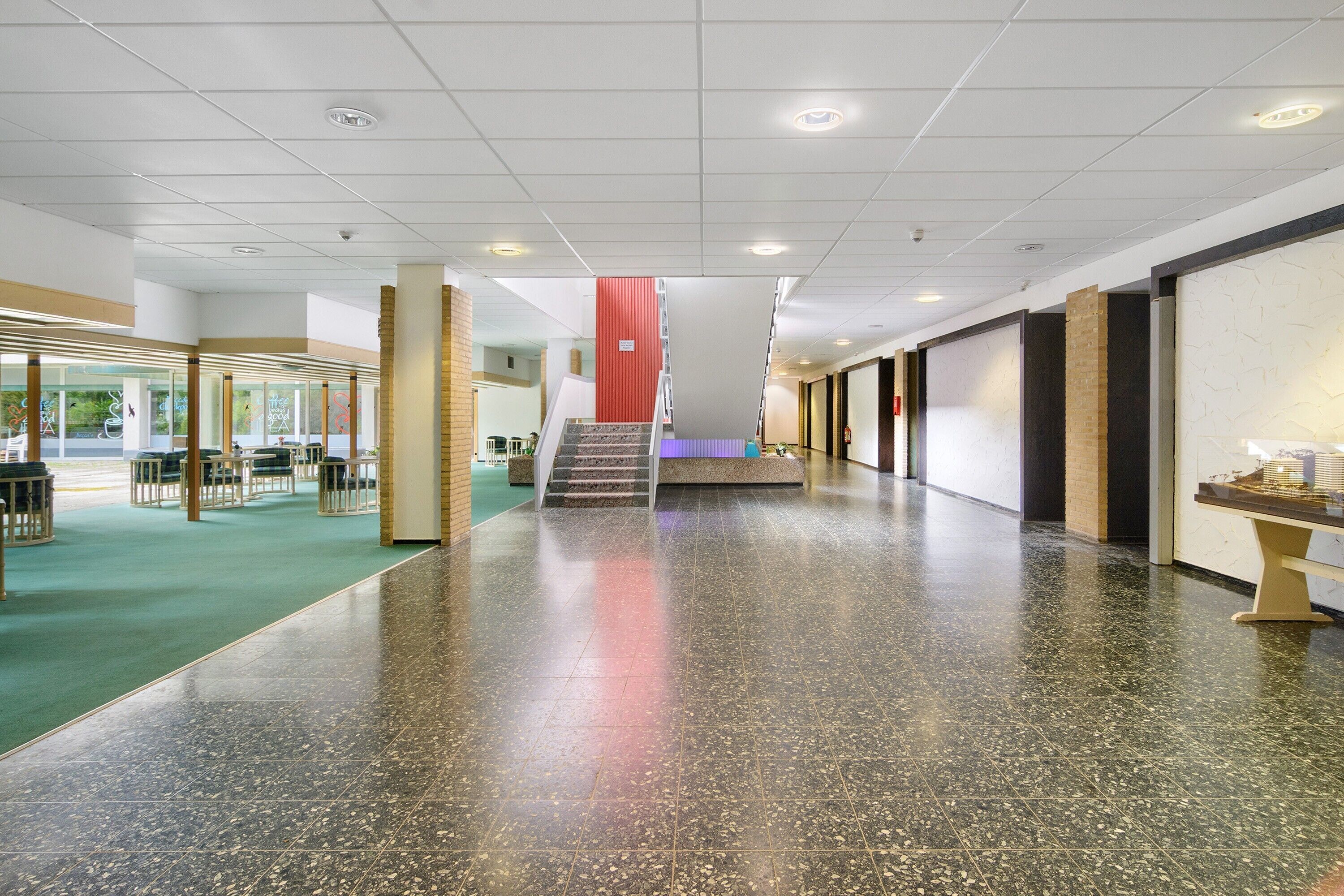 A spacious indoor area with a polished floor, a staircase, and a seating area with tables and chairs.
