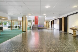 Um espaço amplo e interno, com piso lustroso, uma escada e uma área de estar com mesas e cadeiras.