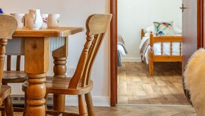 A wooden dining table with chairs, a bed with a colorful pillow, and a painting on the wall. - 3 Bed in Umberleigh (oc-78305) (Kings Nympton)
