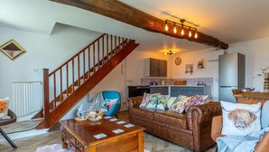 A living room with a wooden staircase, a sofa, a coffee table, and a kitchen in the background. - 3 Bed in Umberleigh (oc-78305) (Kings Nympton)