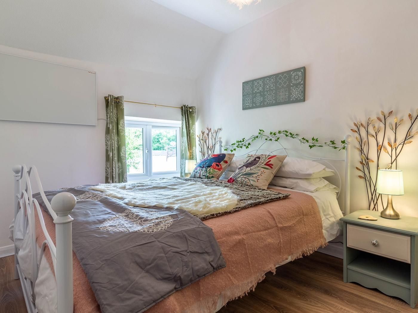 Une chambre à coucher avec un lit, une table de chevet, une lampe et une fenêtre avec des rideaux.