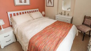 Een slaapkamer met een bed, nachtkastje, dressoir, stoel, spiegel en twee wanddecoraties.