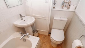 Een badkamer met een bad, wastafel, toilet en een klein plankje met een welkomstbord en een decoratie van een reddingsboei.