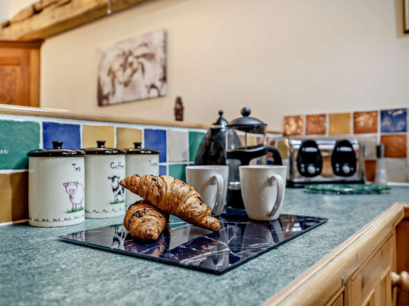 A kitchen counter with a croissant, a coffee pot, and a mug.