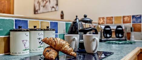 A kitchen counter with a croissant, a coffee pot, and a mug.