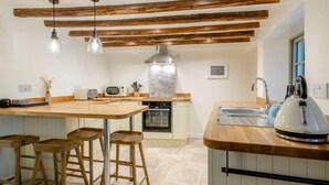 Una cocina con vigas de madera, una isla central con taburetes, un microondas, un tostador y un hervidor.