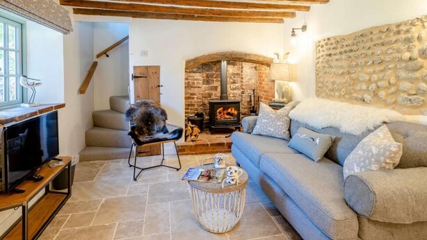 Una sala de estar acogedora con vigas de madera a la vista, una chimenea de piedra, un sofá y un televisor.