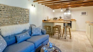 Una sala de estar acogedora con un sofá, una pared de piedra y una zona de cocina con estufa y taburetes de bar.