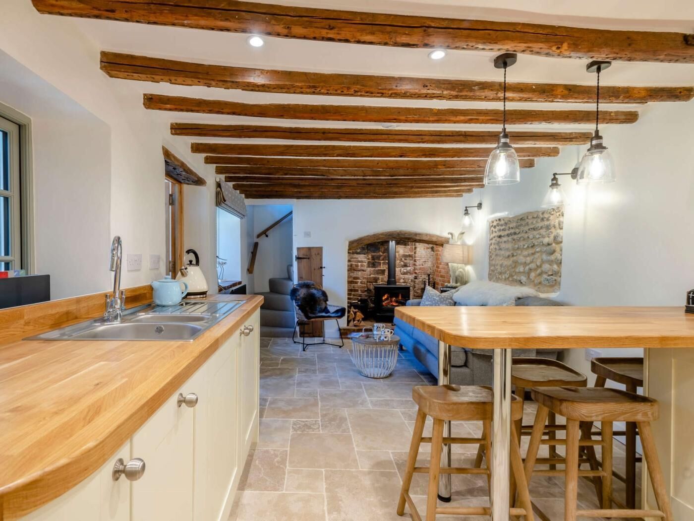 Una cocina rústica con vigas de madera a la vista, una chimenea de piedra y una zona de comedor de madera con taburetes de bar.