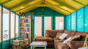A cozy room with a green ceiling, a brown sofa, a bookshelf, and a bicycle. - 2 Bed in Umberleigh (oc-78303) (Kings Nympton)