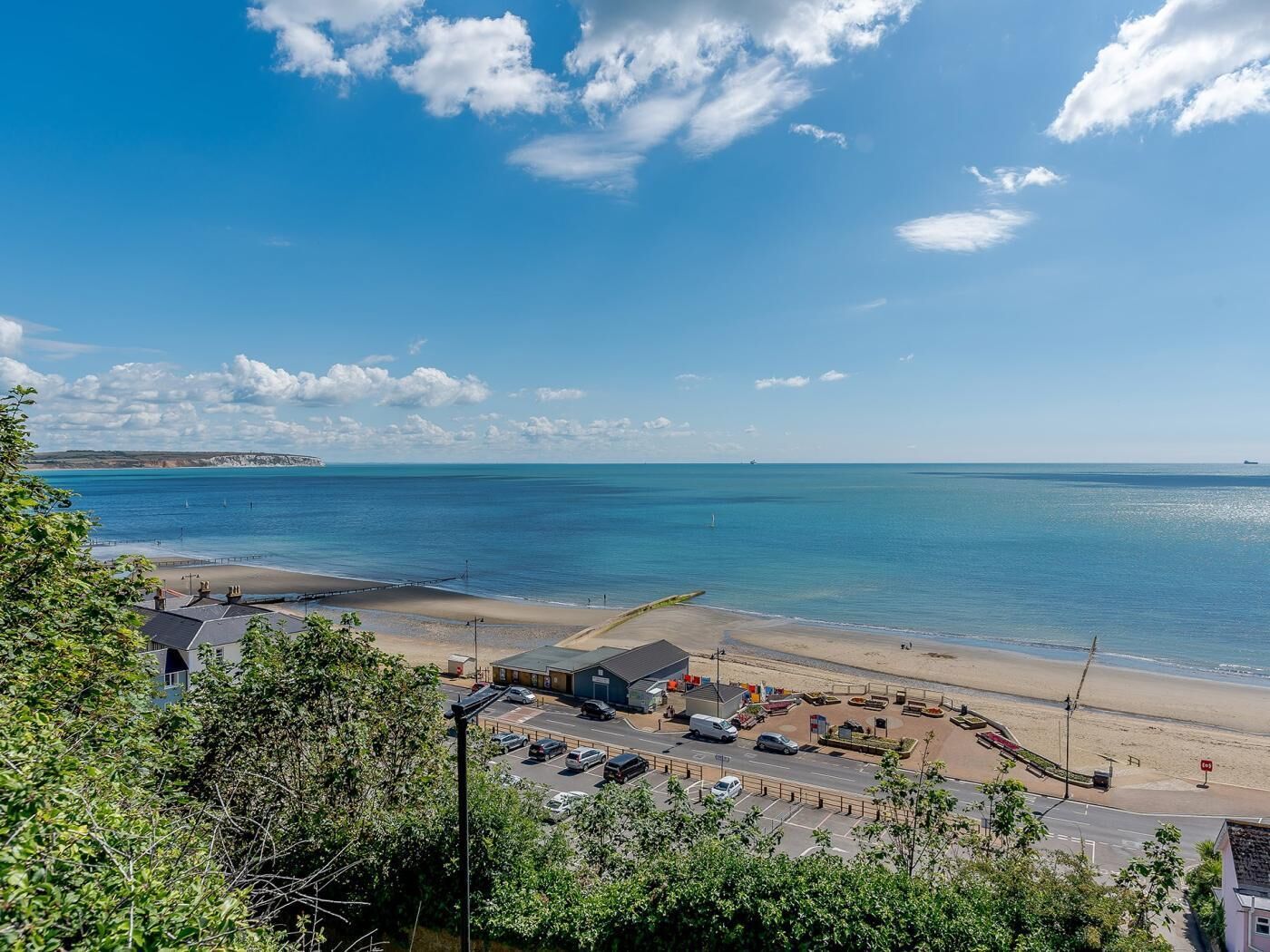 Une vue côtière avec une plage, un espace de stationnement et des bâtiments au premier plan.