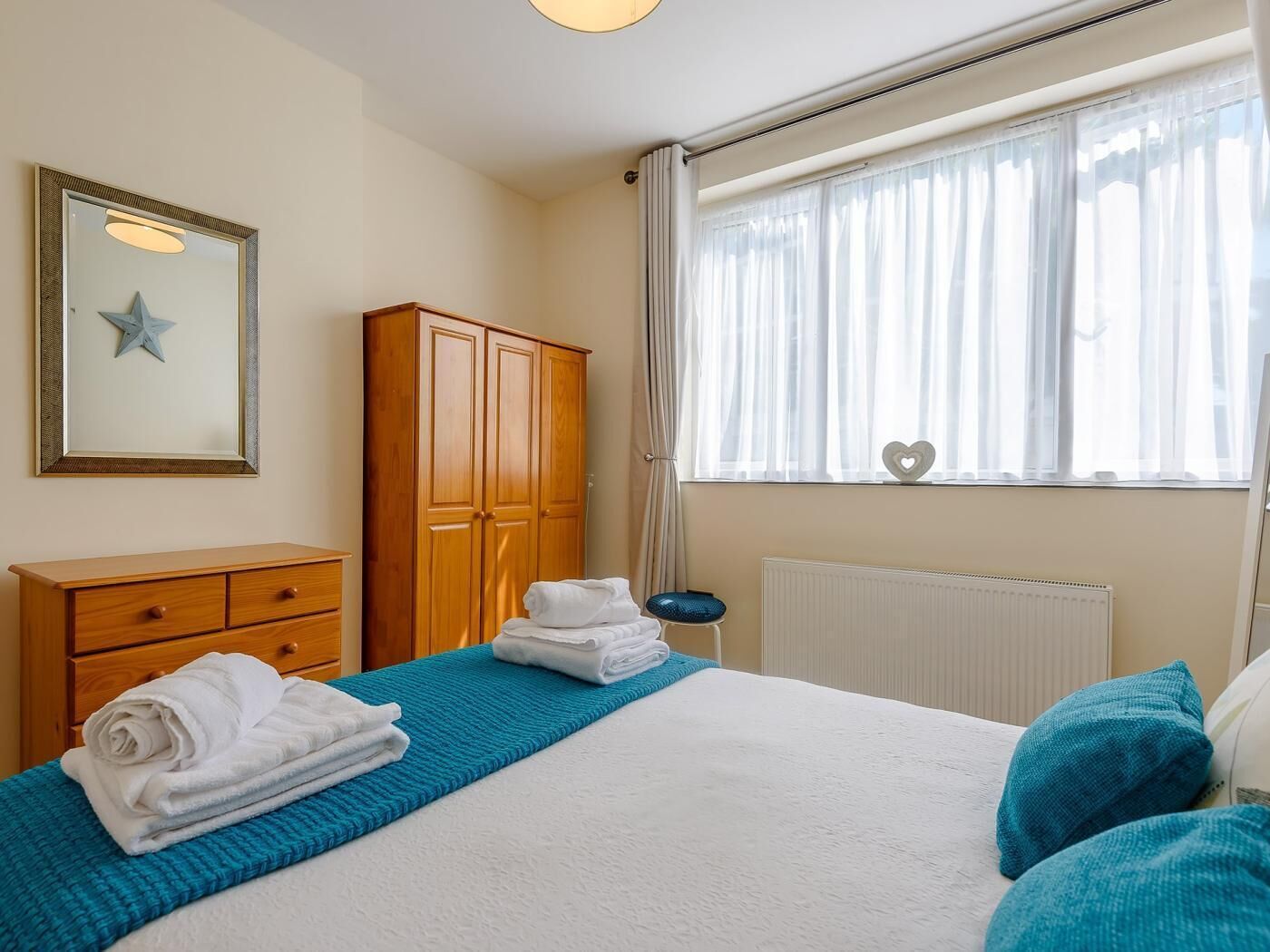 A bedroom with a bed, a wooden wardrobe, a radiator, and a window with curtains.