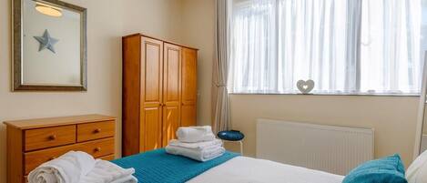 A bedroom with a bed, a wooden wardrobe, a radiator, and a window with curtains.