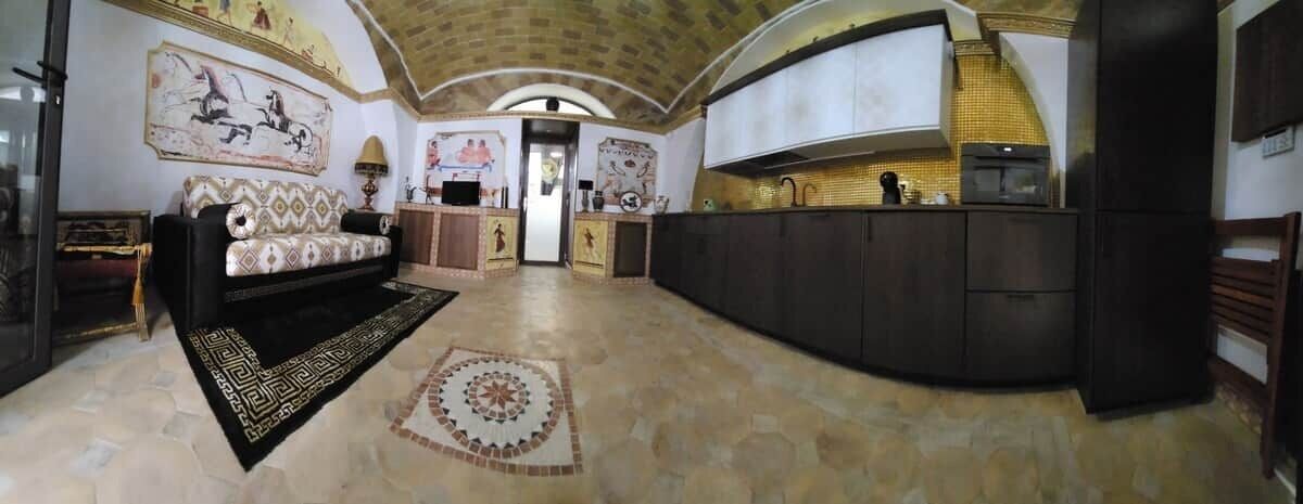 Un área de estar amplia con sofá, un tapete y una cocina con alacenas oscuras y salpicadero de azulejos.