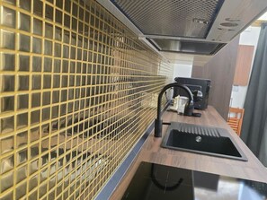 A kitchen with a stainless steel sink, a black faucet, and a yellow grid-patterned partition. - The Etrurian Rapsody (Rome)