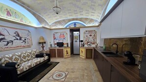 Uma sala de estar ampla, com sofá, mesa de centro, cozinha com pia e bancada, e teto decorativo.