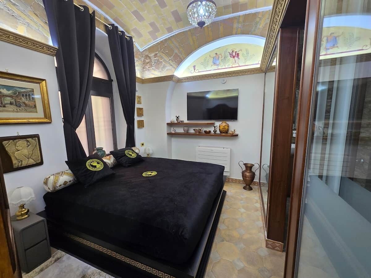 A bedroom with a large bed, a television, a decorative ceiling, and a view of the bathroom.