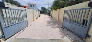 A narrow pathway flanked by high walls and metal gates, leading to a building with a flat roof. - Come for the beaches? Villa Marcos, unique 2-bedrooms apartment Curacao with AC (Willemstad)