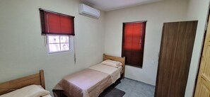 A small, single-bed room with two windows, a door, and an air conditioning unit. - Come for the beaches? Villa Marcos, unique 2-bedrooms apartment Curacao with AC (Willemstad)
